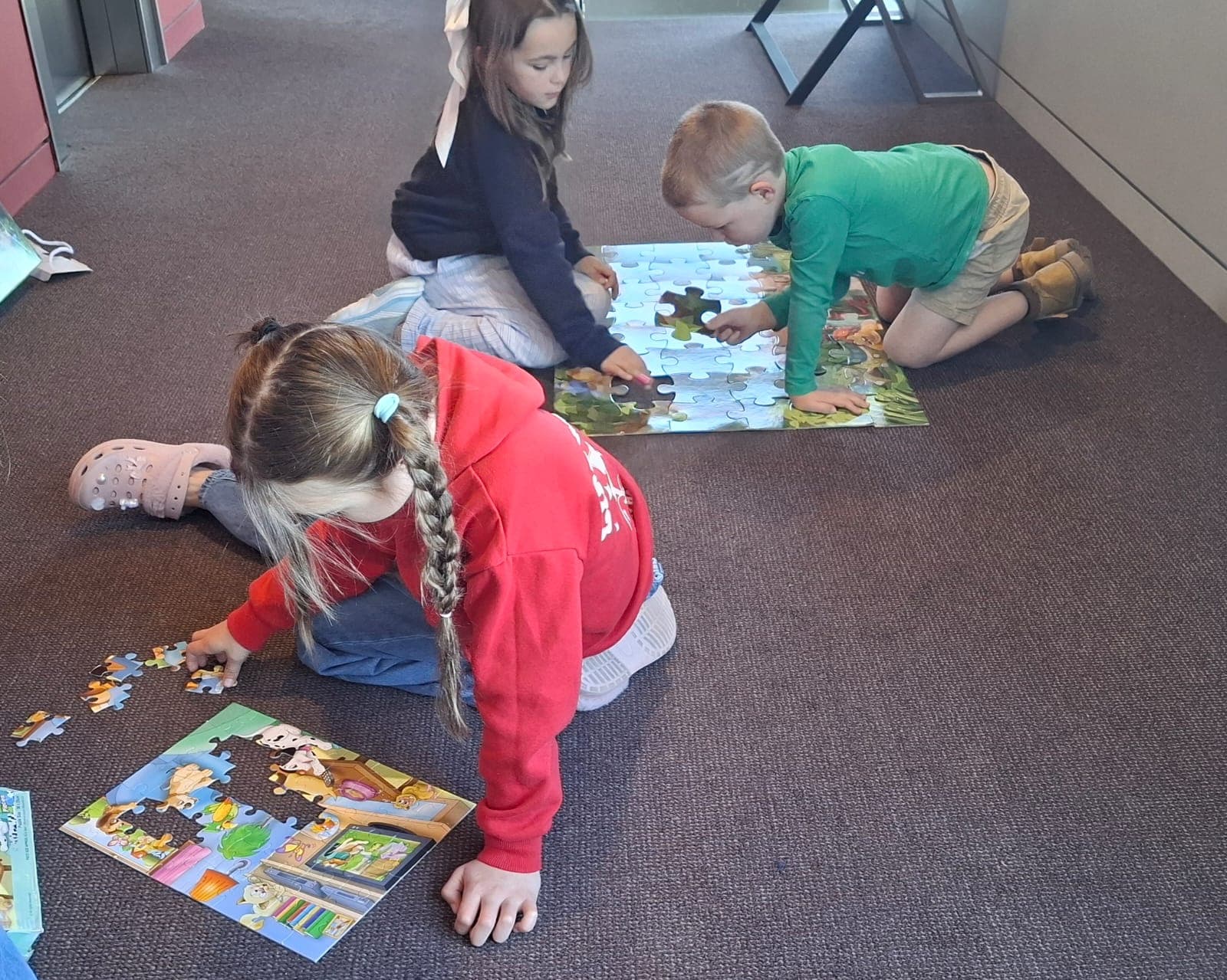 Three children sitting on the floor putting together jigsaw puzzles.