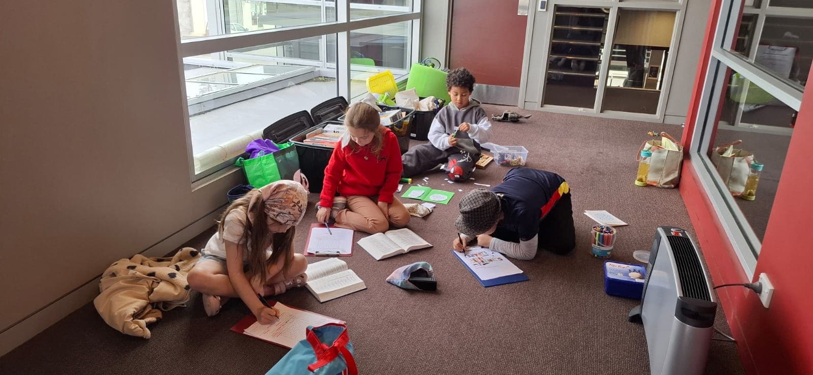 Four children spread out on the floor with open books and colouring pages.
